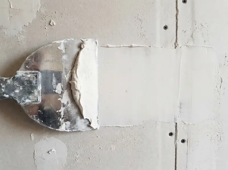 Brede roestvrijstalen plamuurmes met vulmiddel dat over een wand wordt getrokken